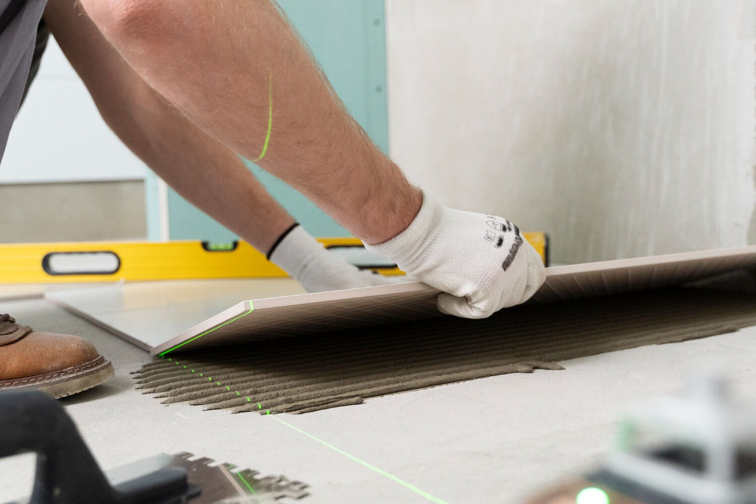 Person installing a floor tile with adhesive and using a level tool