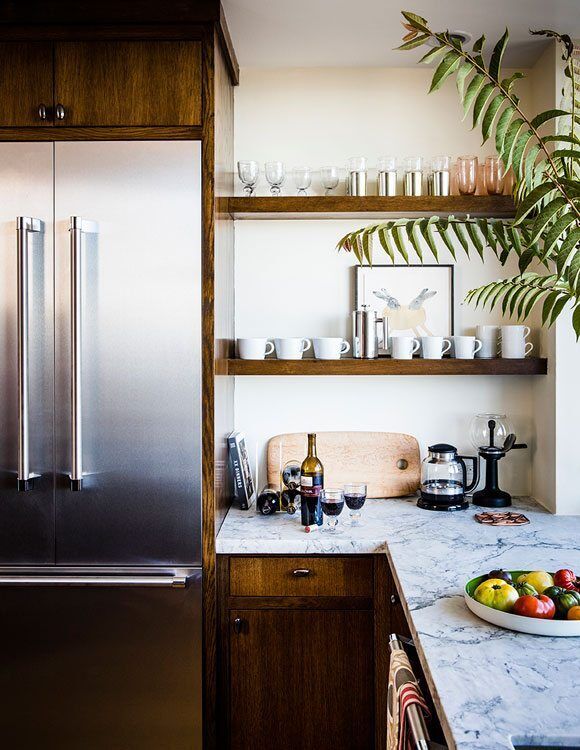 Kitchen corner with stainless steel fridge, wooden shelves, and marble countertop with fruit bowl