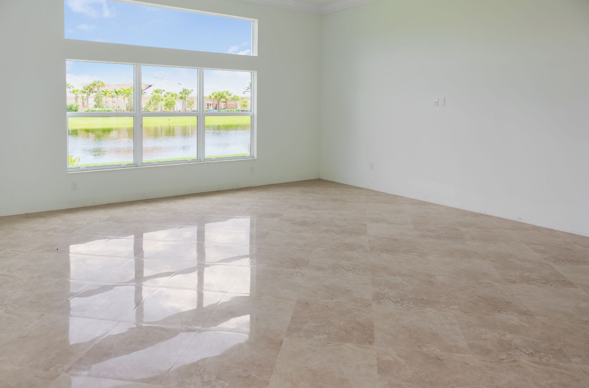 Empty room with large windows and polished porcelain tile floor overlooking a pond