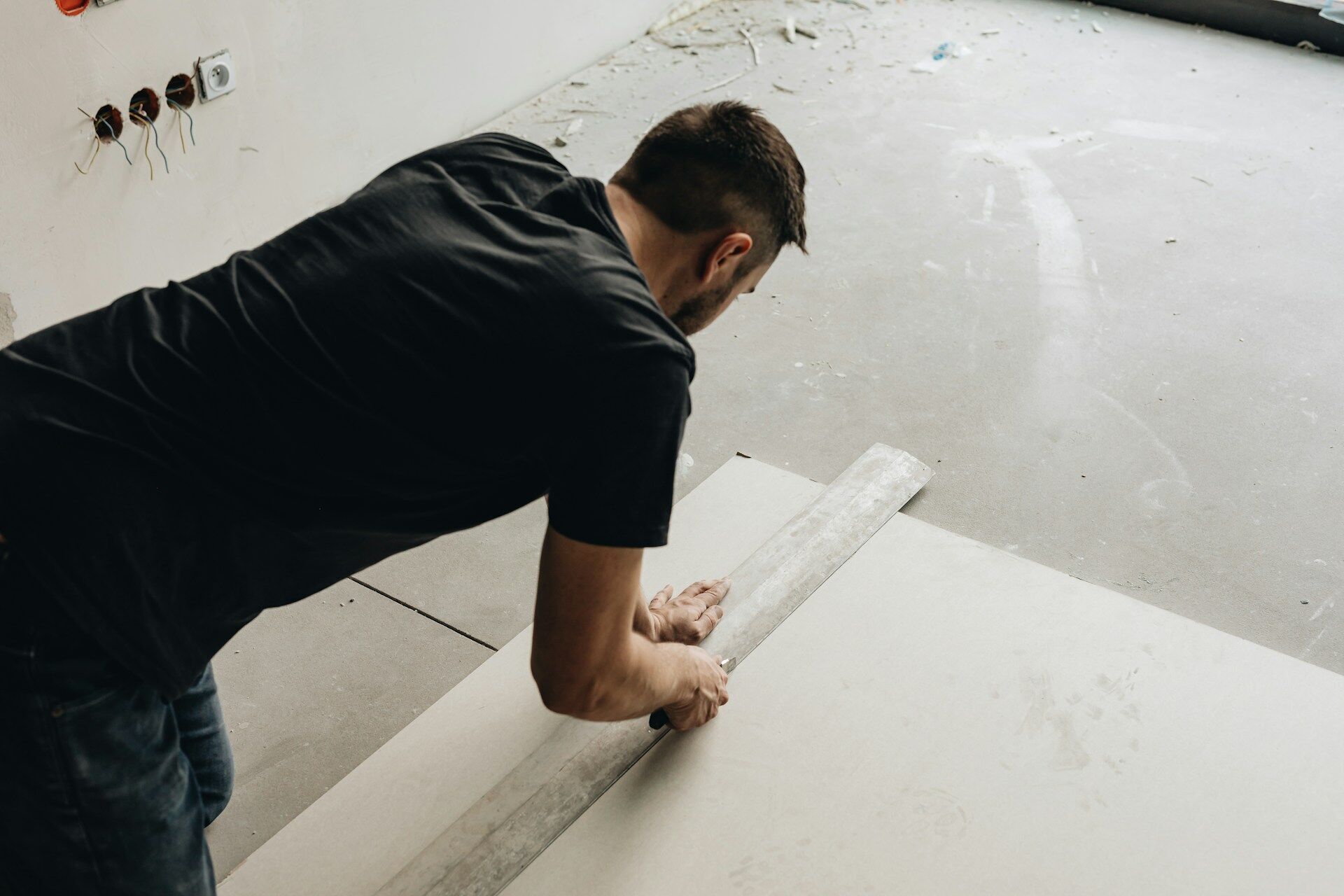 Person measuring a large tile or board on the floor with a straightedge tool in a construction area