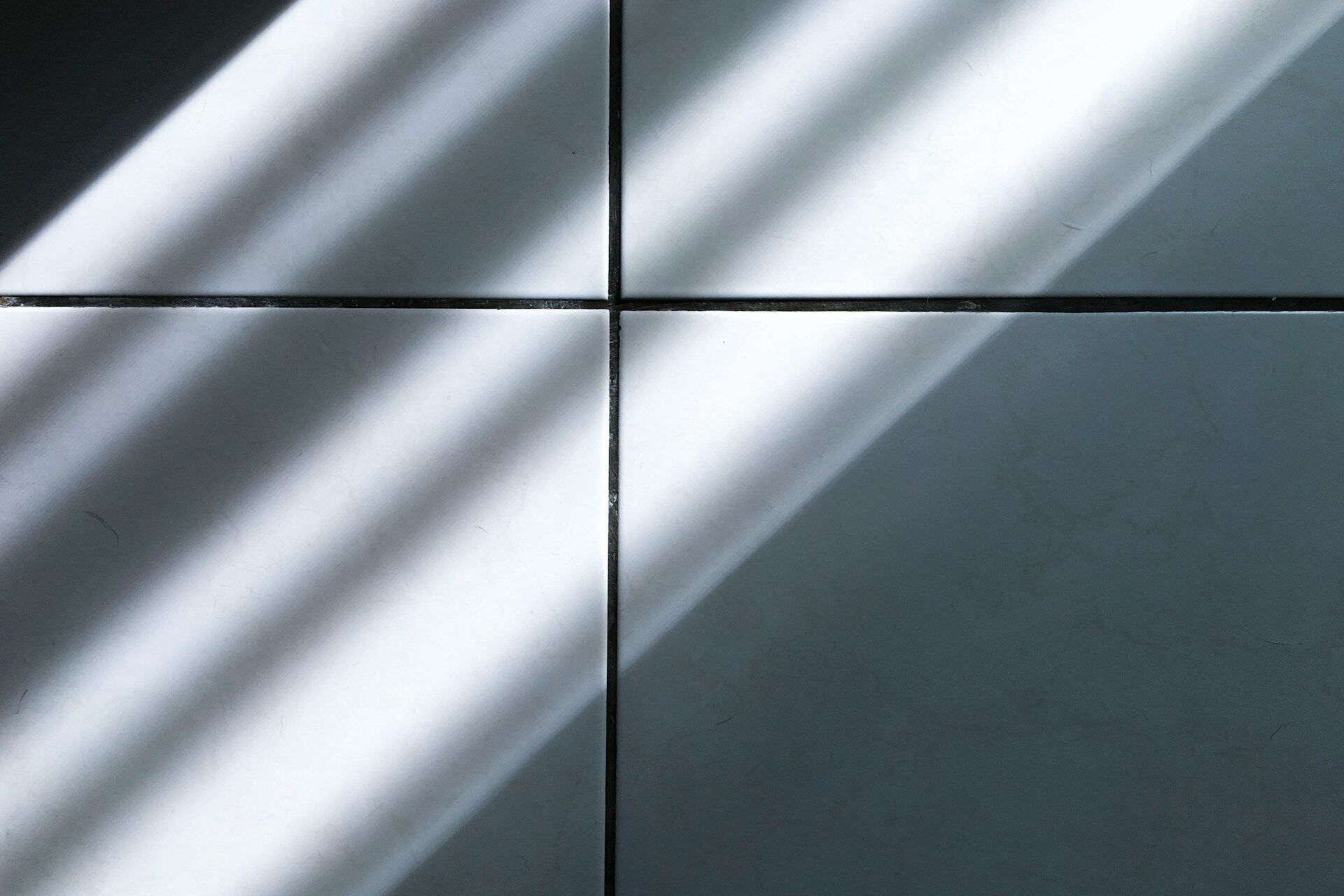 Close-up of four white tiles with grout lines and shadows across the surface