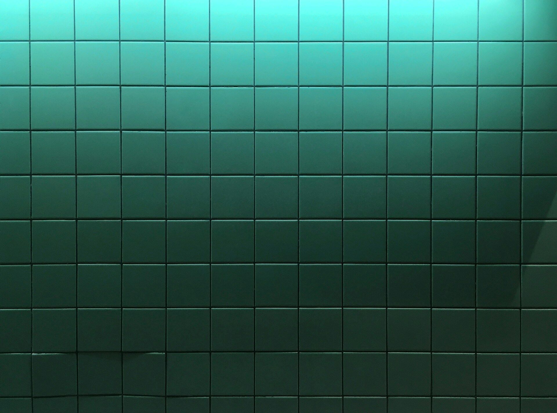 Wall of green square tiles with visible grout lines in a grid pattern
