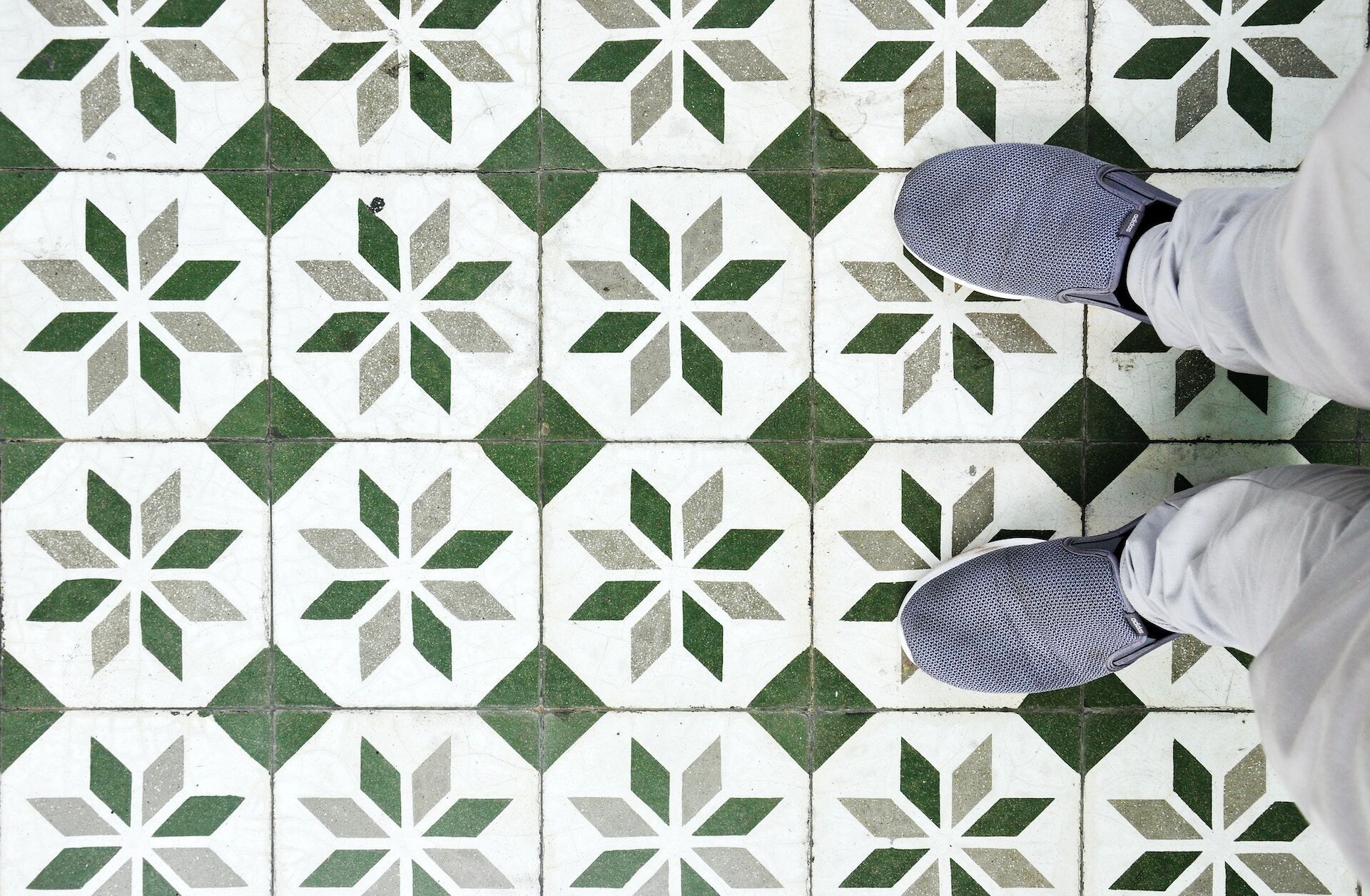 Top-down view of geometric star pattern tiles in green and white with gray shoes visible