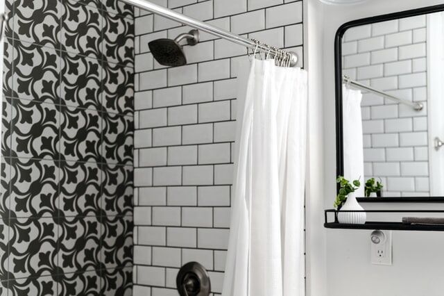 Bathroom featuring white subway tiles and black patterned tiles with a shower curtain and mirror