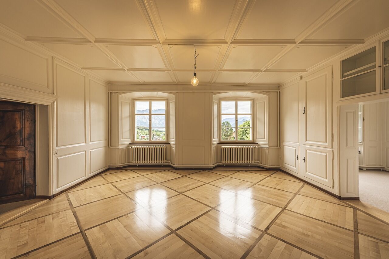 Empty room with wooden flooring, white walls, and large windows showing a scenic view
