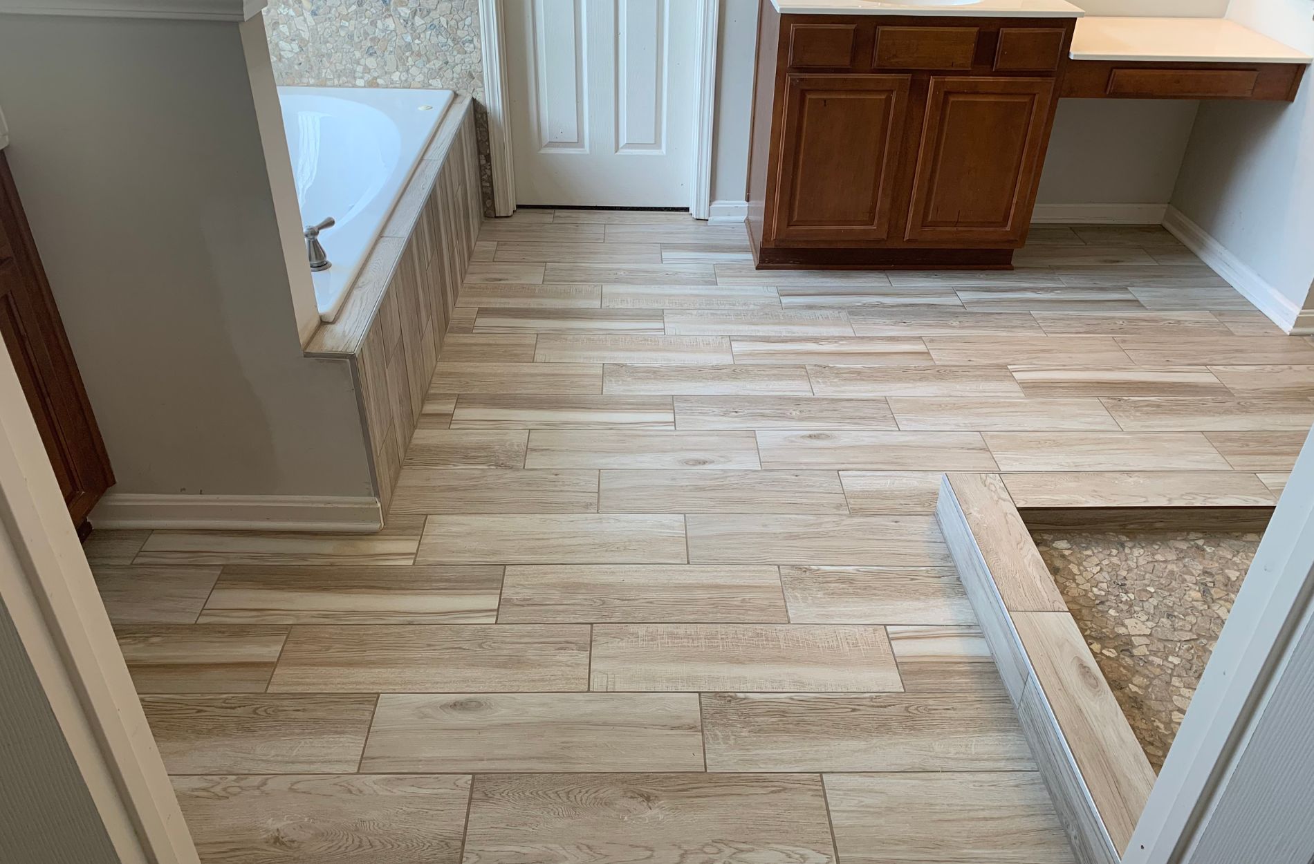 Bathroom with wood-look tile flooring, bathtub, and wooden vanity