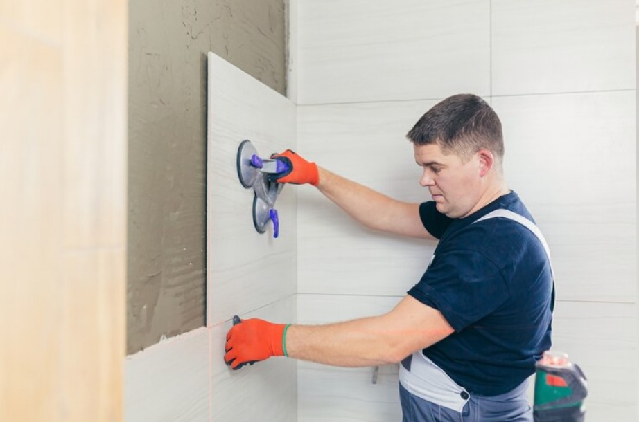 Worker installing large-format light-colored tiles on a bathroom wall with suction tools