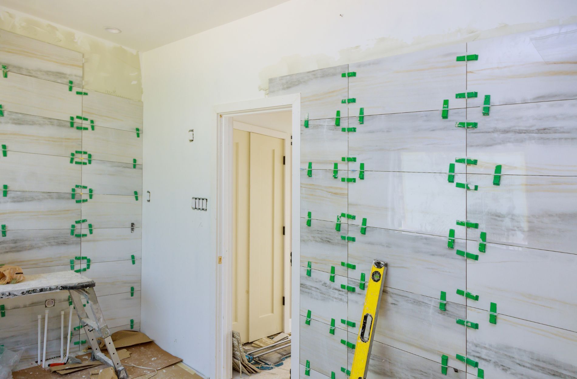 Bathroom under renovation with large-format marble tiles and green spacers on the walls