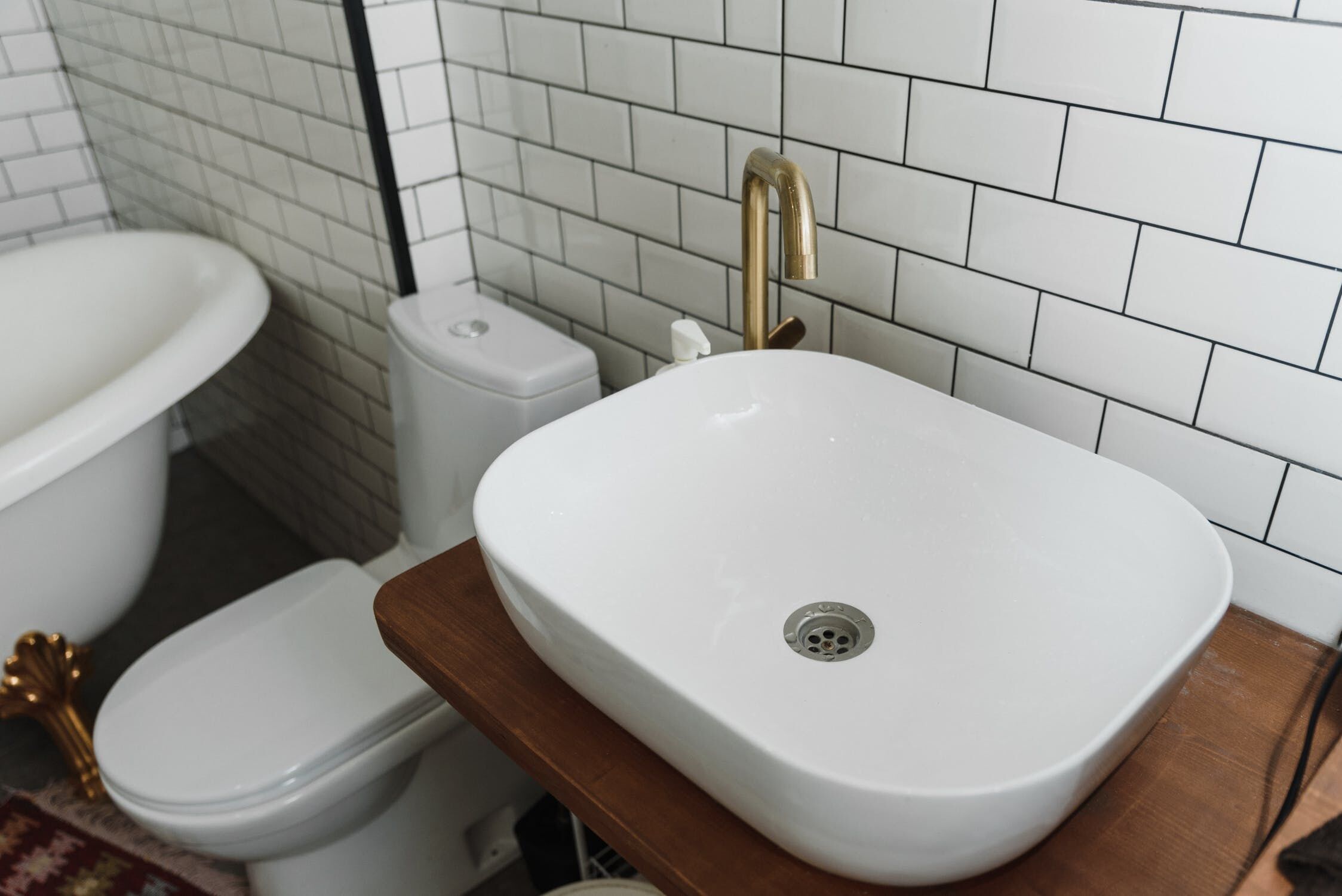 Bathroom with white sink, gold faucet, toilet, and freestanding bathtub with subway tile walls