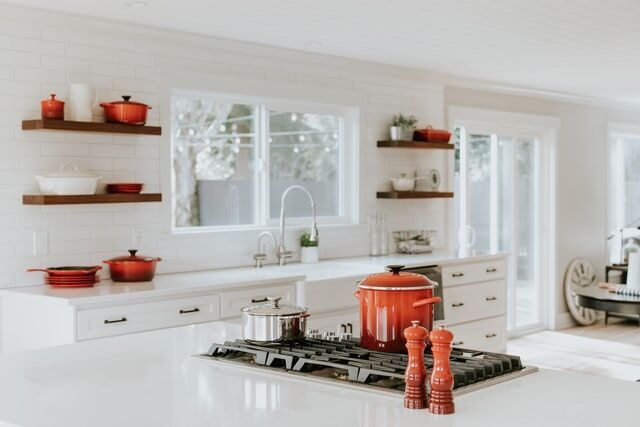 Modern kitchen with white countertops, gas stove, and red cookware on open shelves