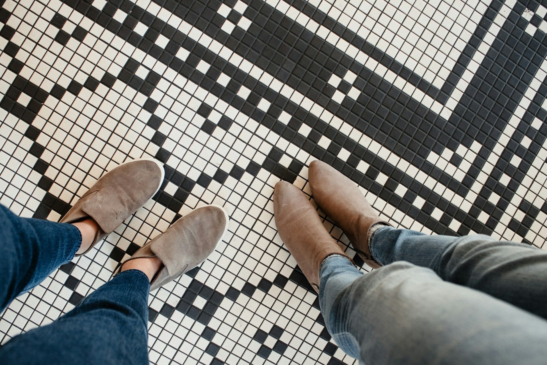 Two people standing on a black and white mosaic tile floor with a geometric pattern