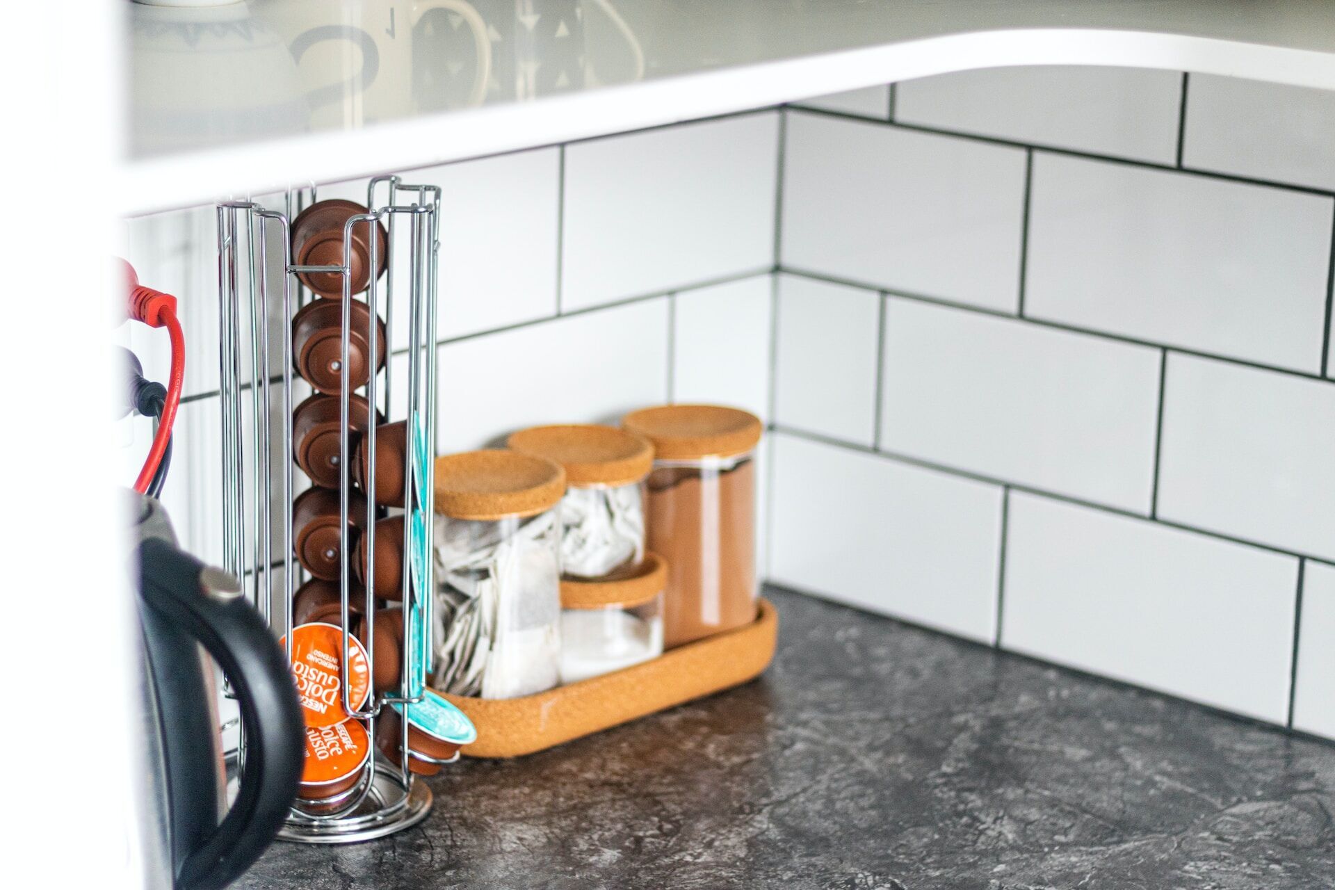 Kitchen countertop with coffee pod holder and jars against white subway tile backsplash