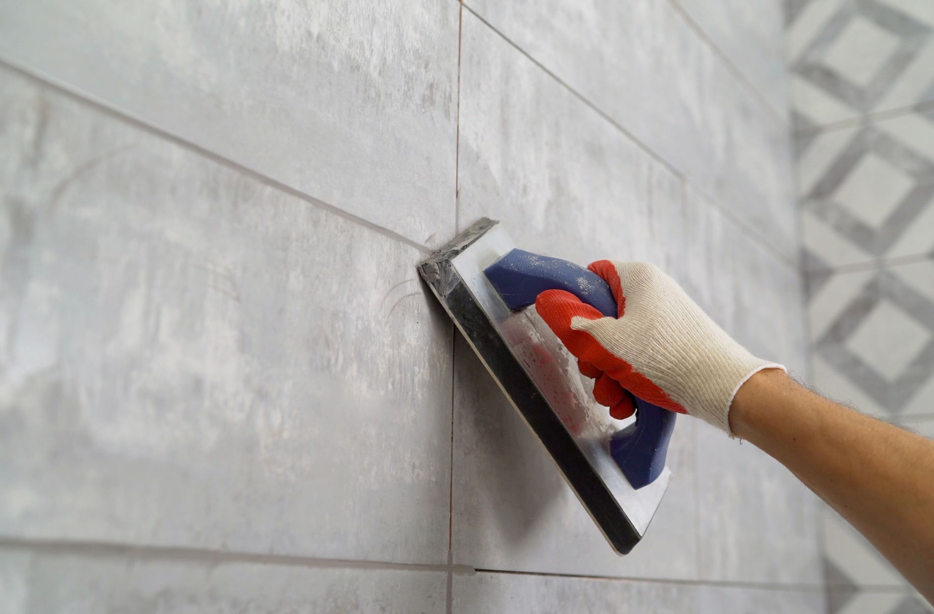 Gloved hand applying grout to ceramic tile wall with a grout float