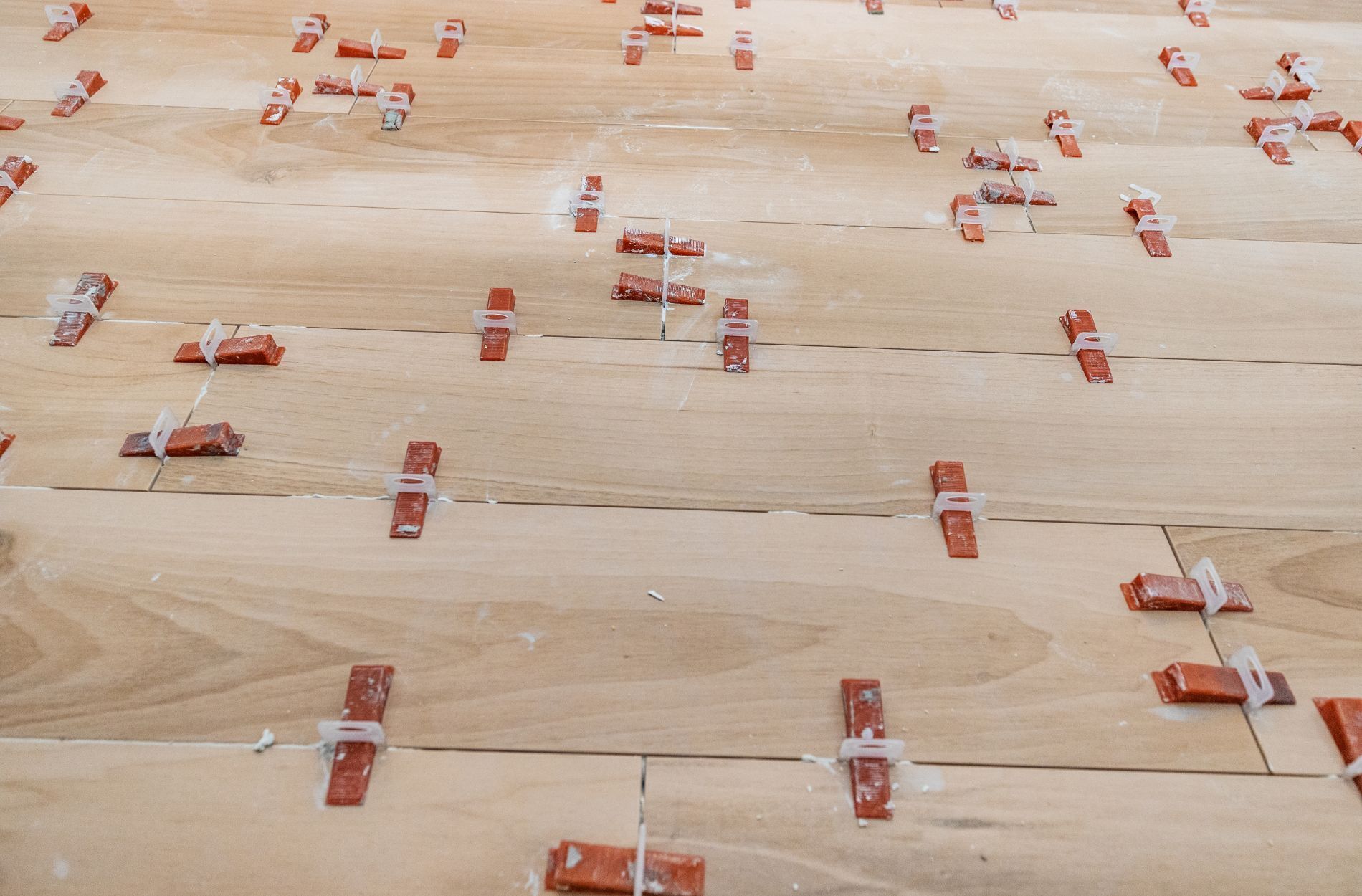 Close-up of ceramic tiles being installed with red spacers and leveling clips on a floor