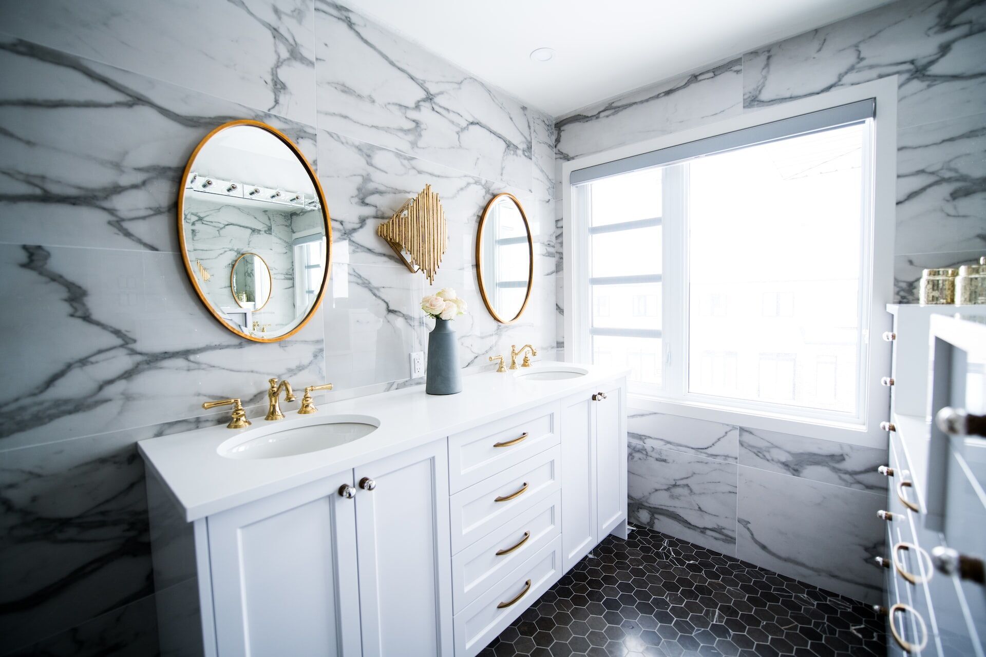 Modern bathroom with marble tile walls, double vanity, and gold fixtures under natural light