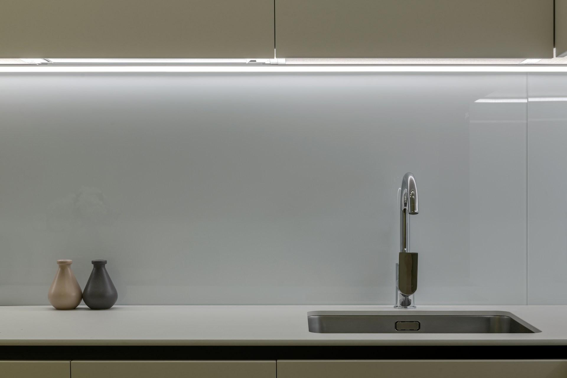 Modern kitchen countertop with a sleek faucet and two decorative vases against a minimalist backsplash