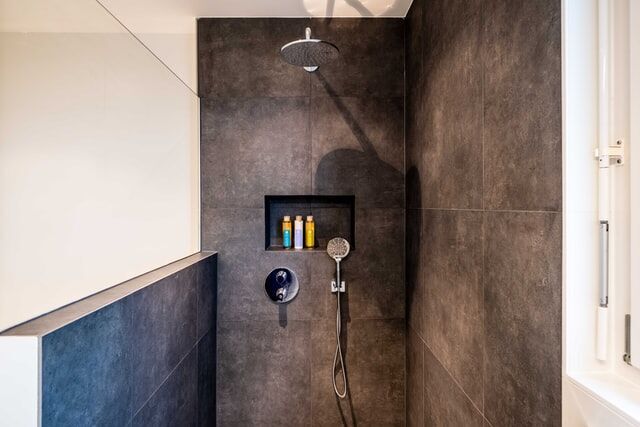 Modern shower with dark tiles, rainfall showerhead, and built-in niche with toiletries