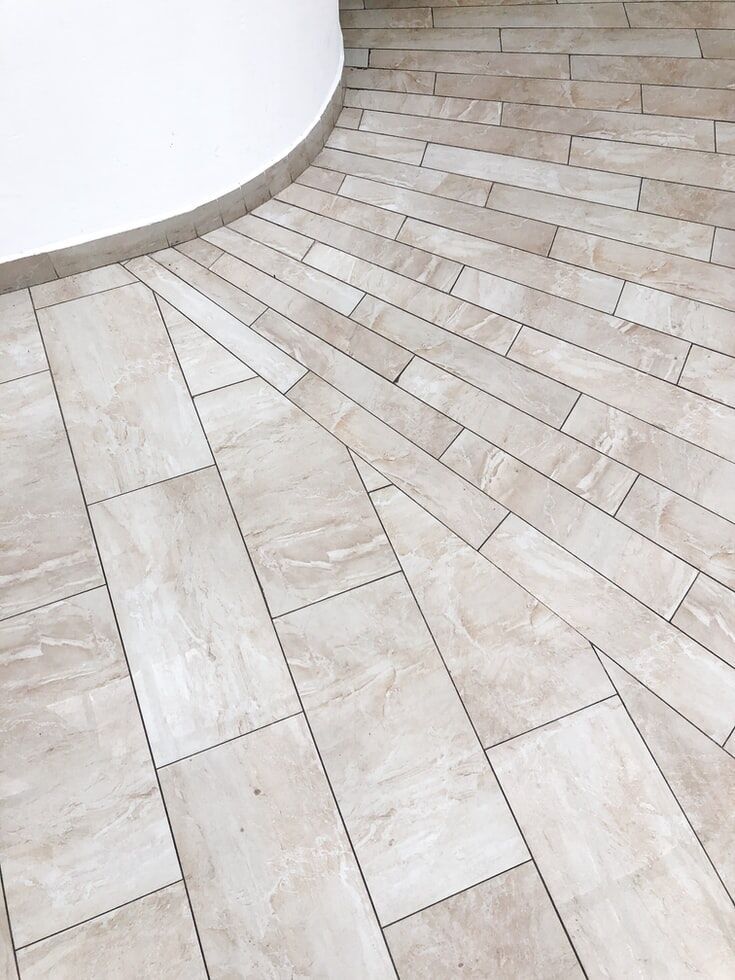 Beige rectangular floor tiles arranged around a curved wall, showcasing a unique pattern