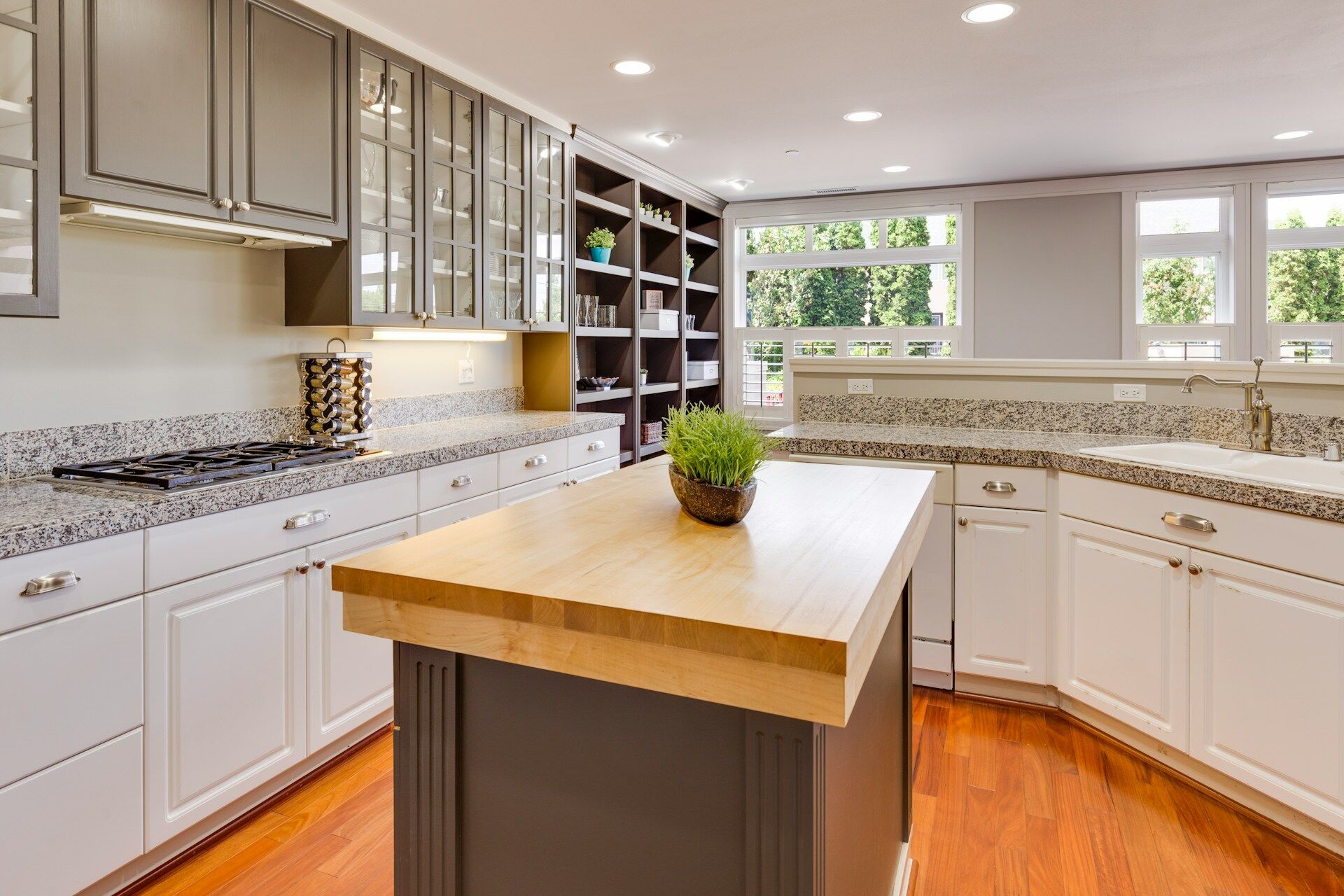 Modern kitchen with granite countertop, wooden island, and white cabinets under large windows