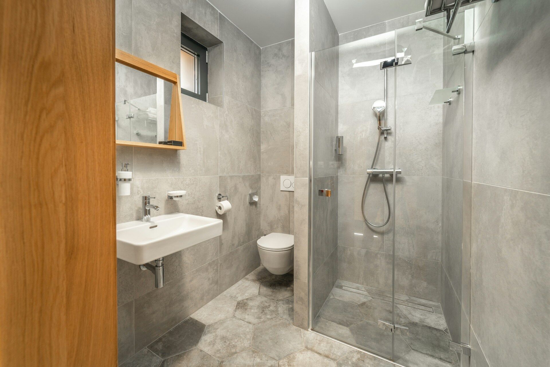 Modern bathroom featuring hexagonal floor tiles, wall-mounted sink, toilet, and glass shower enclosure