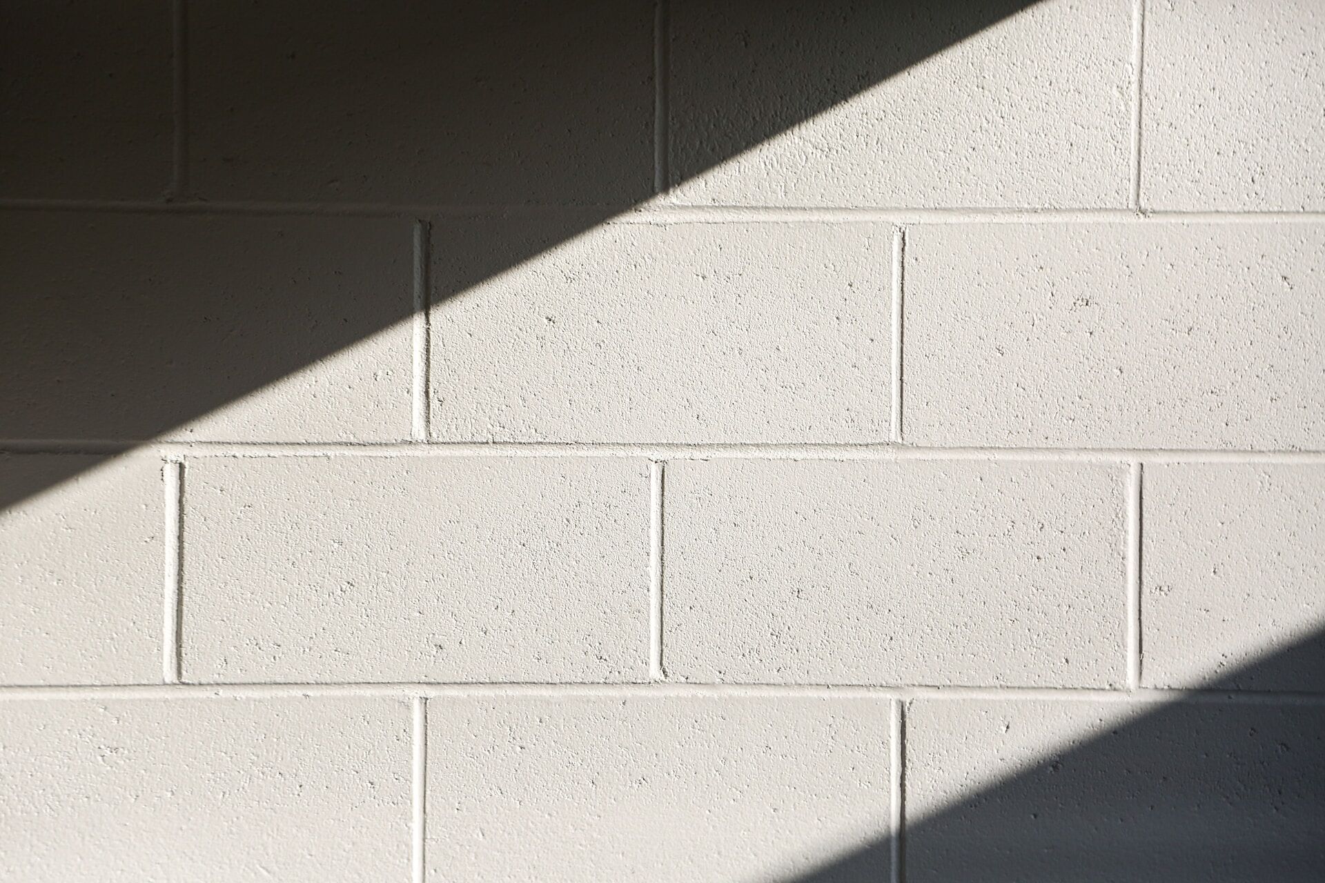 Close-up of a white brick wall with diagonal shadows, highlighting texture and pattern