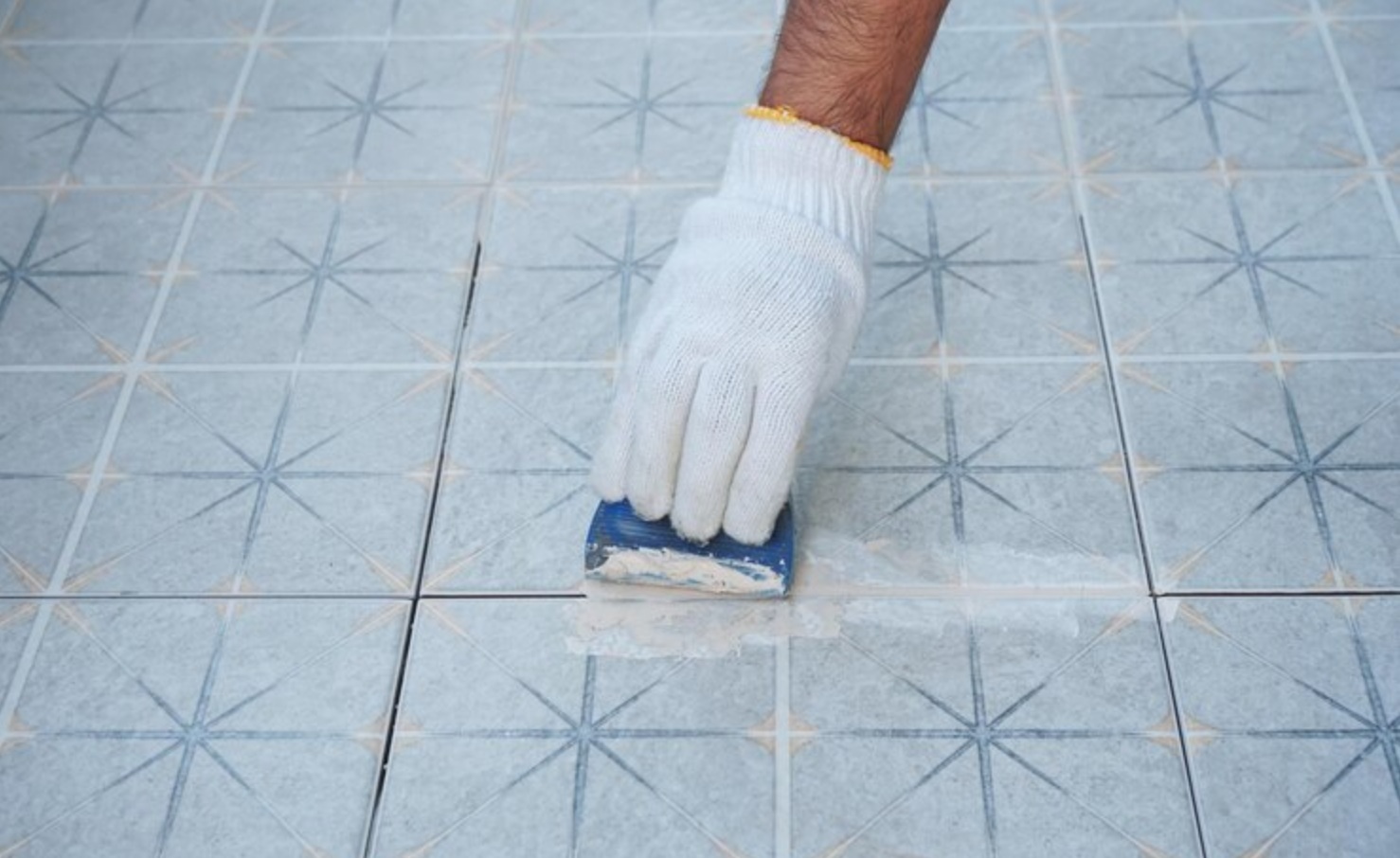 Person applying grout to light blue patterned tiles with a grout float and white glove
