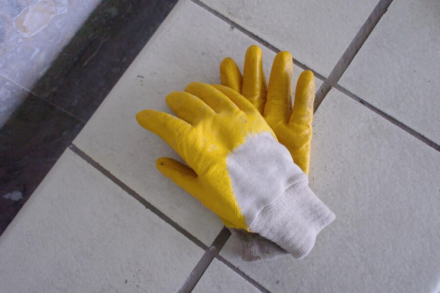 Yellow work gloves on a tiled floor showing grout lines, related to grout maintenance