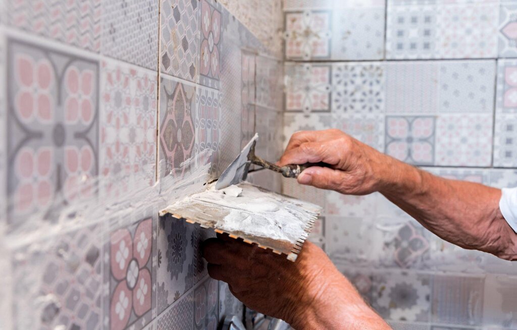 Person applying grout to patterned shower tiles with a trowel, ensuring secure installation