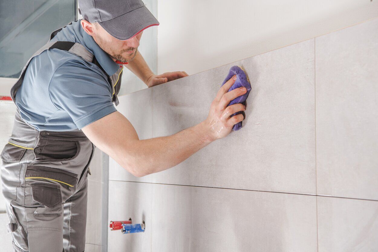 Worker cleaning a tiled wall with a sponge, focusing on grout lines