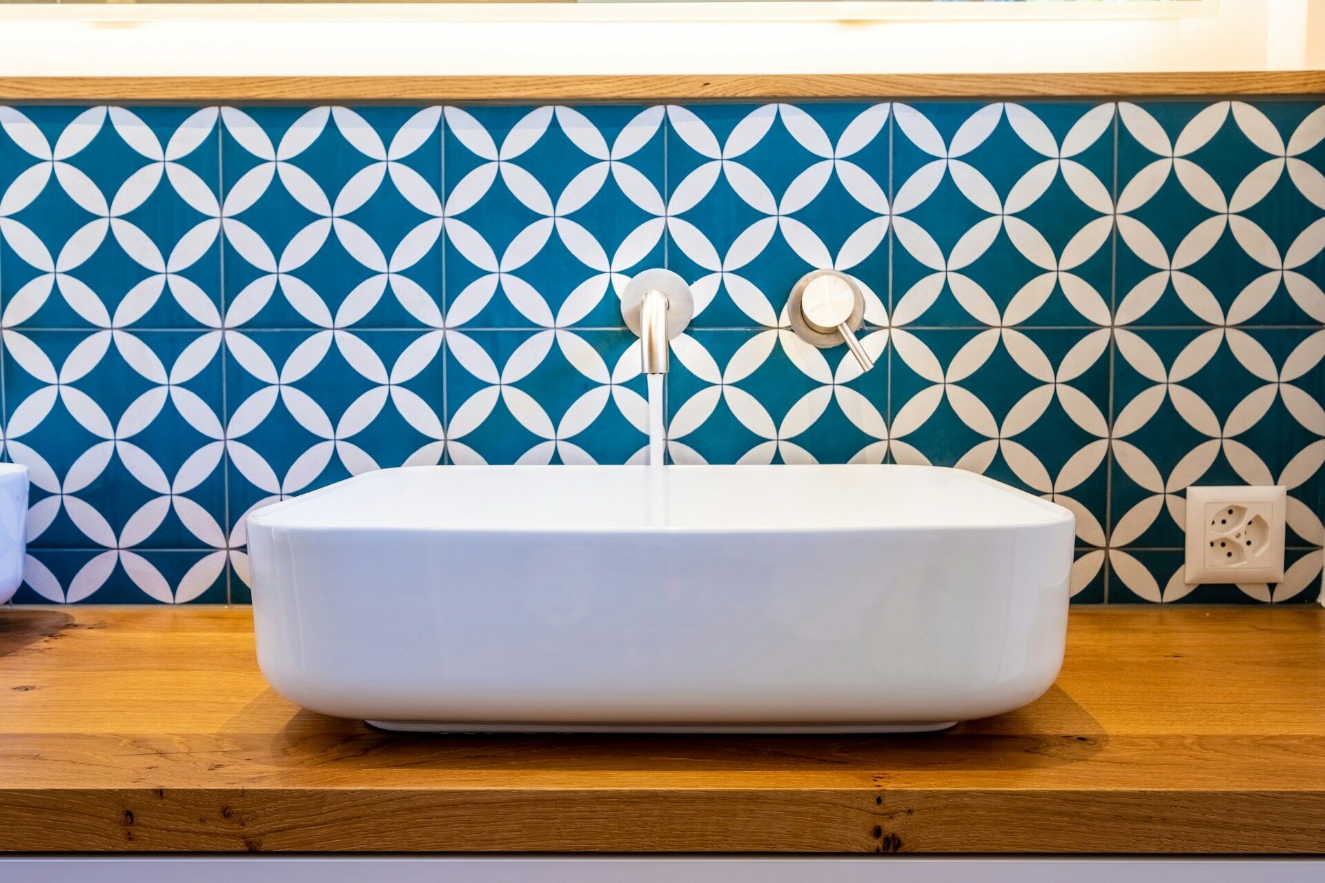 Bathroom sink with blue and white geometric tile backsplash and wooden countertop