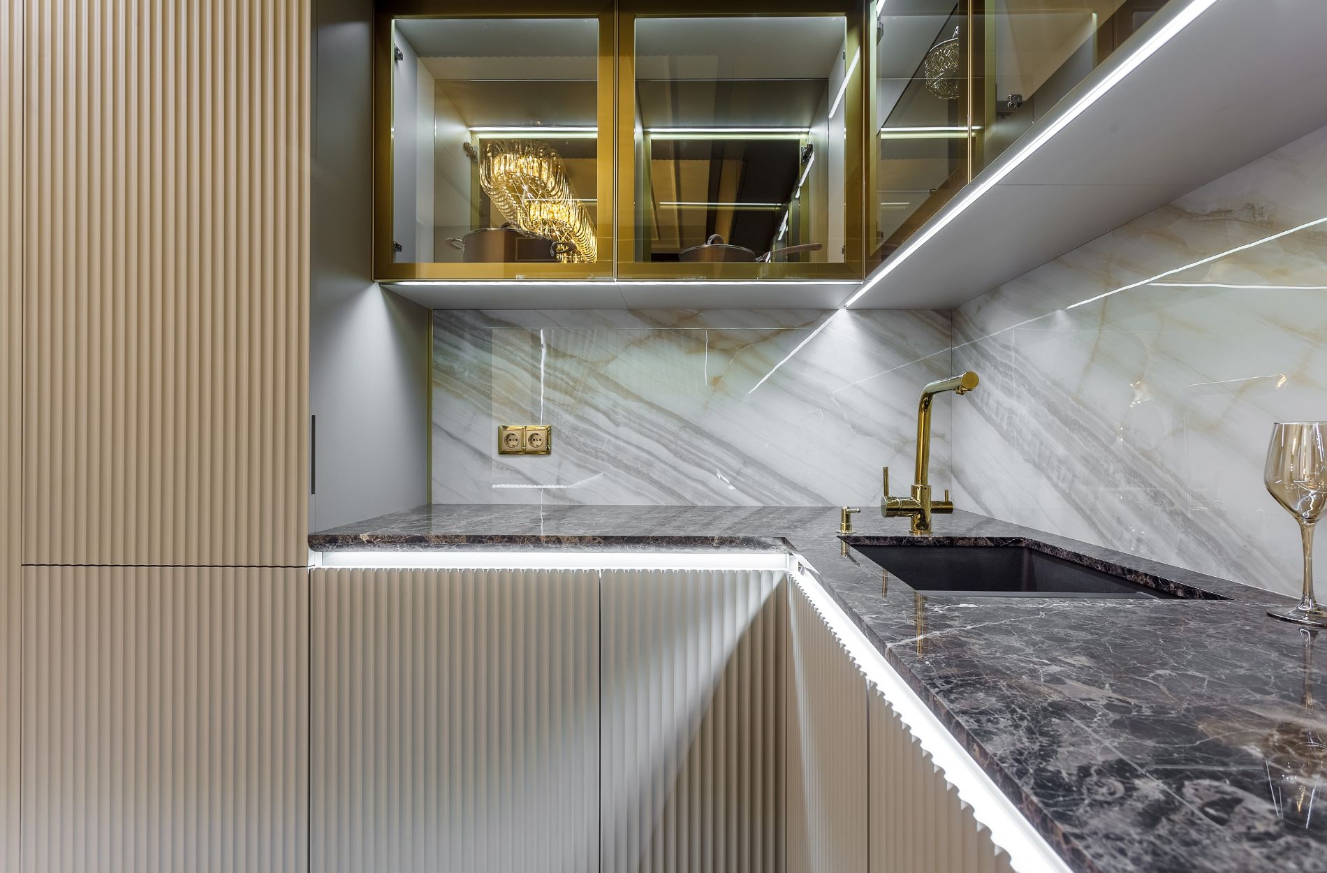 Modern kitchen featuring a dark stone countertop, gold faucet, and marble backsplash with glass cabinets above