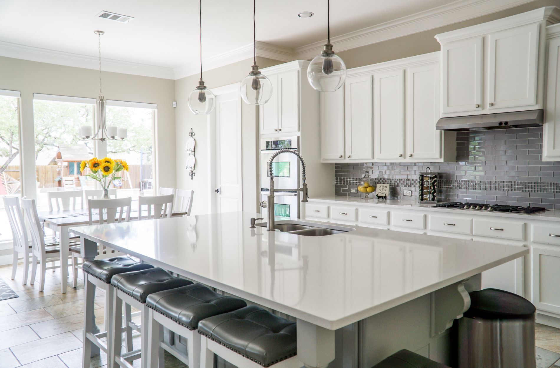 Modern kitchen with white quartz island, bar stools, white cabinets, and gray tile backsplash
