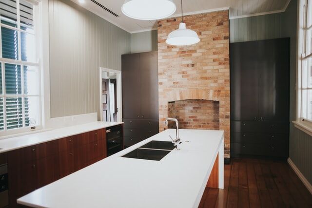 Modern kitchen featuring a white countertop island, brick backsplash, and wooden cabinets with pendant lighting