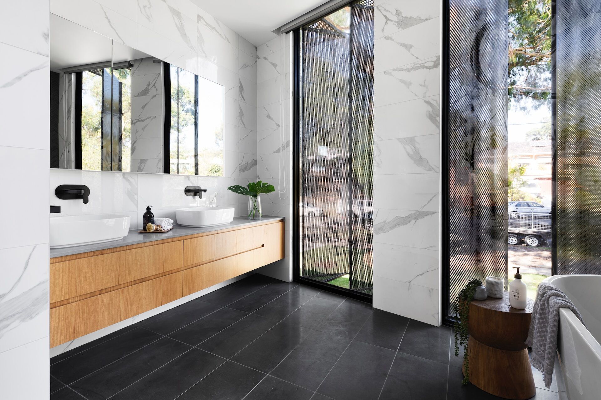 Modern bathroom with double vanity, vessel sinks, and marble tile walls next to large windows