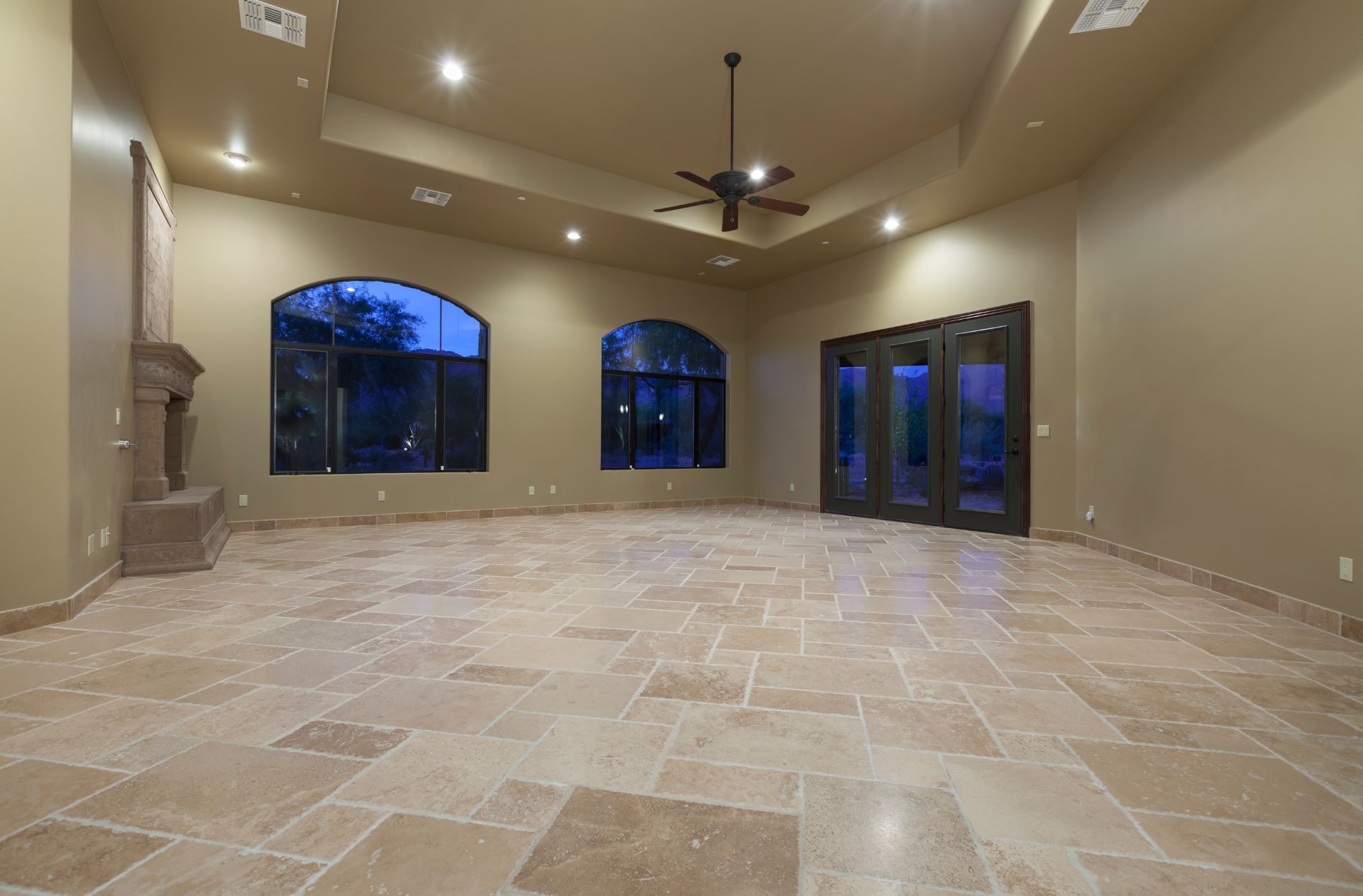 Spacious living room with beige stone tile flooring, large windows, and ceiling fan