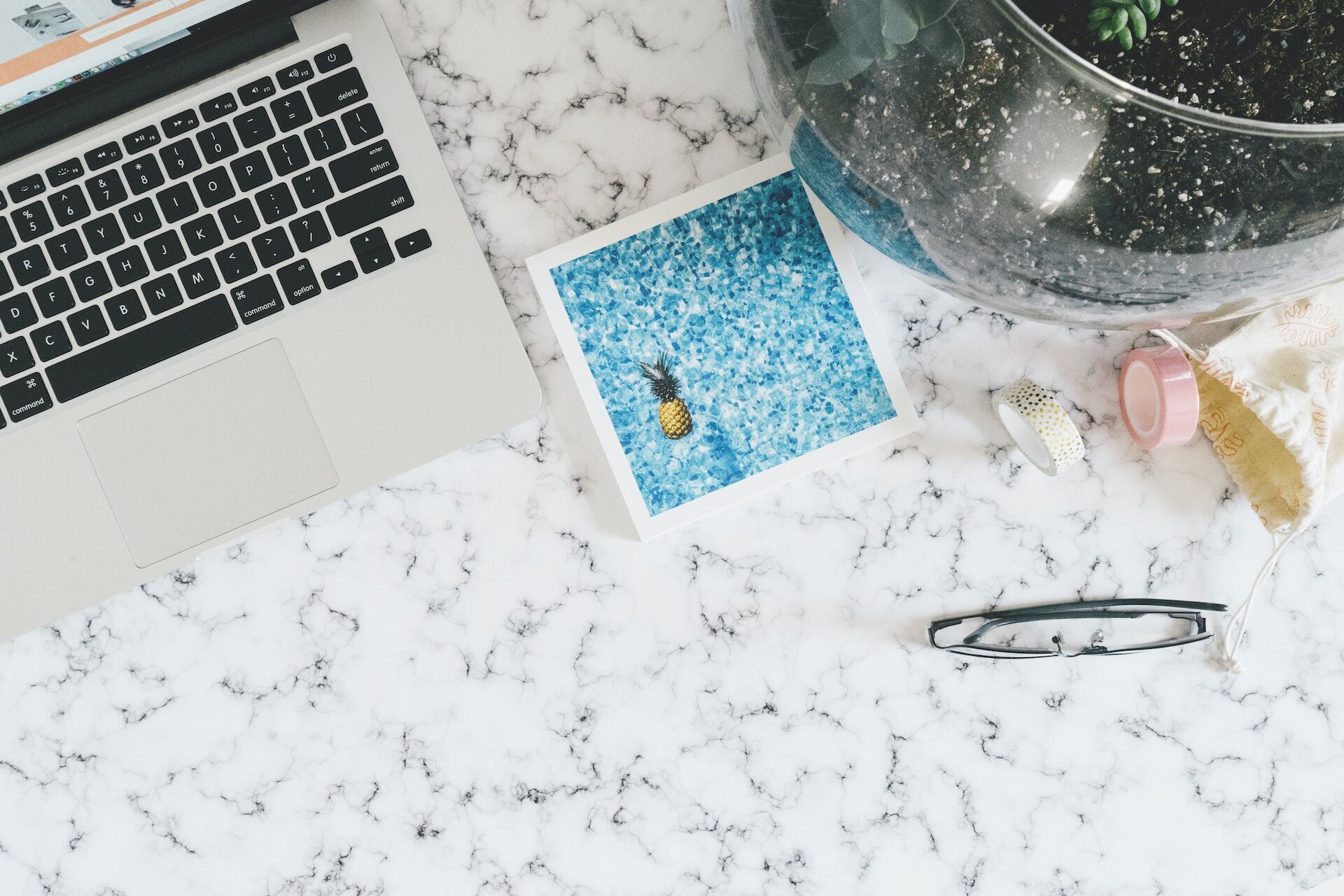 Marble surface with laptop, photo, plant, glasses, and decorative tape