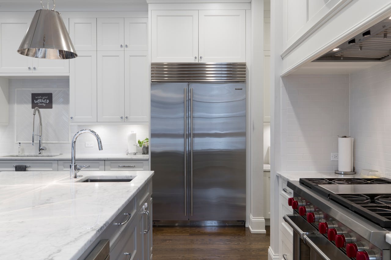 Modern kitchen with marble countertop, stainless steel fridge, and white cabinets