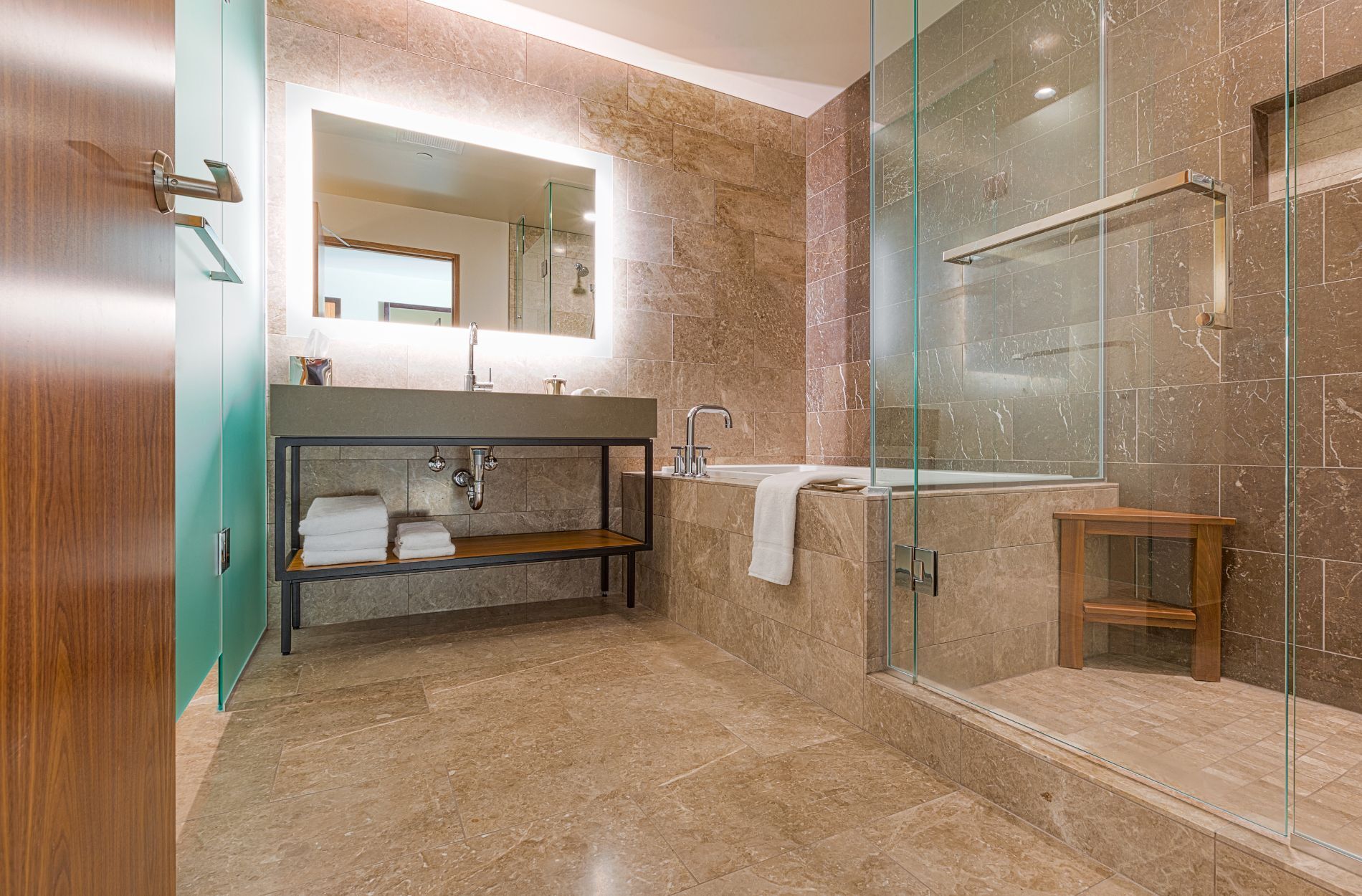 Modern bathroom with glass shower, marble tiles, and backlit mirror
