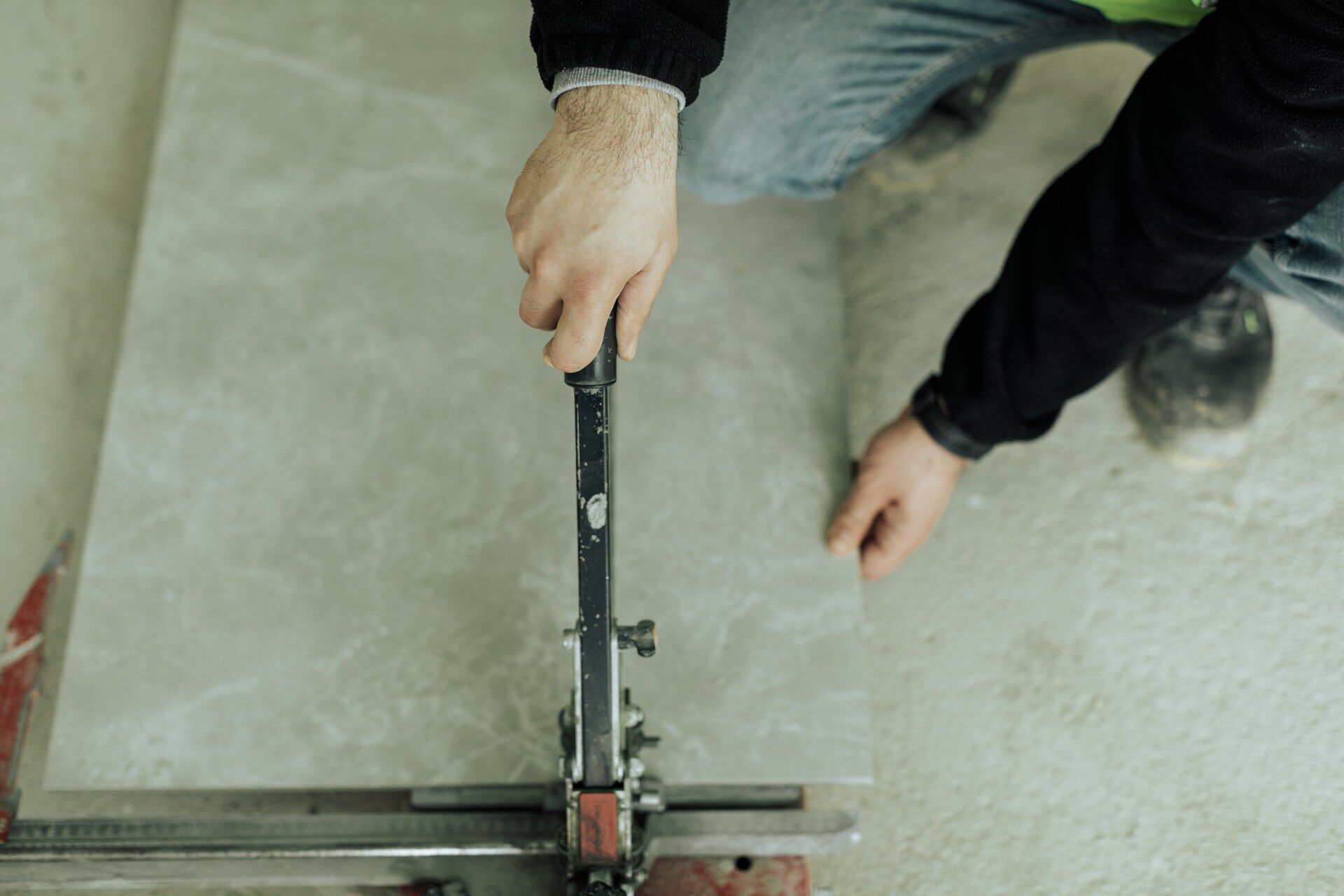Person using a manual tile cutter to cut a large tile on the floor