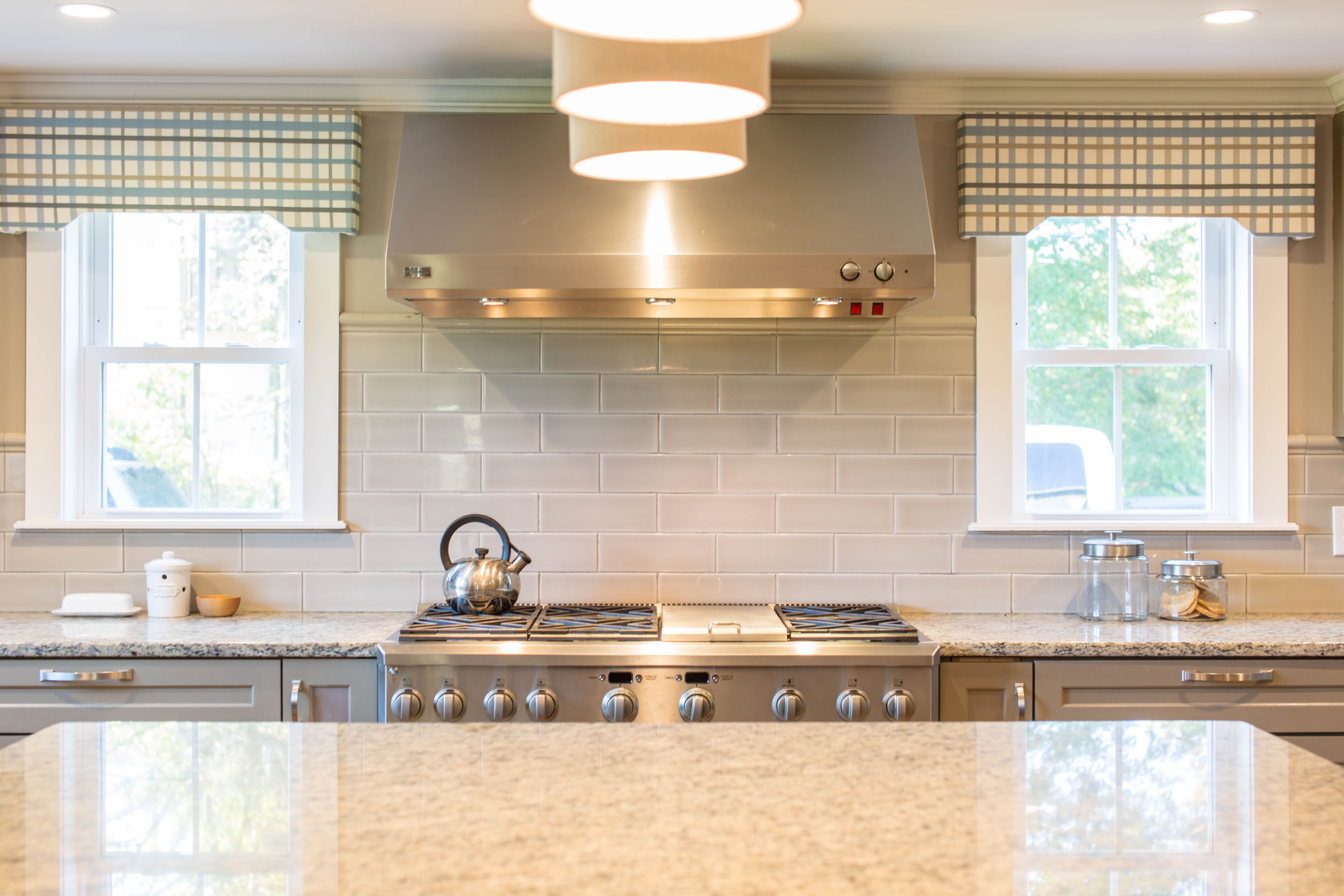 Modern kitchen featuring a granite countertop, stainless steel stove, and subway tile backsplash with windows