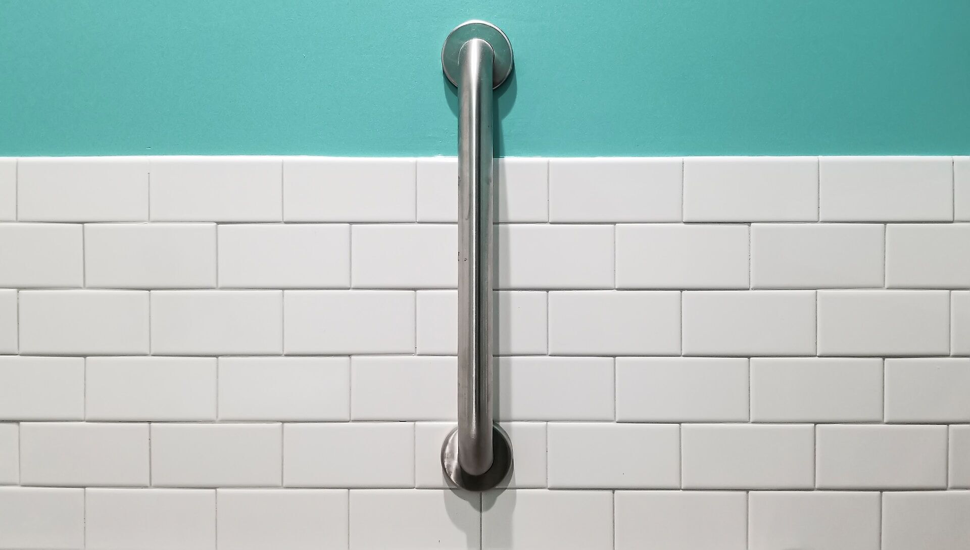 White subway tile wall with a stainless steel grab bar and teal upper wall section