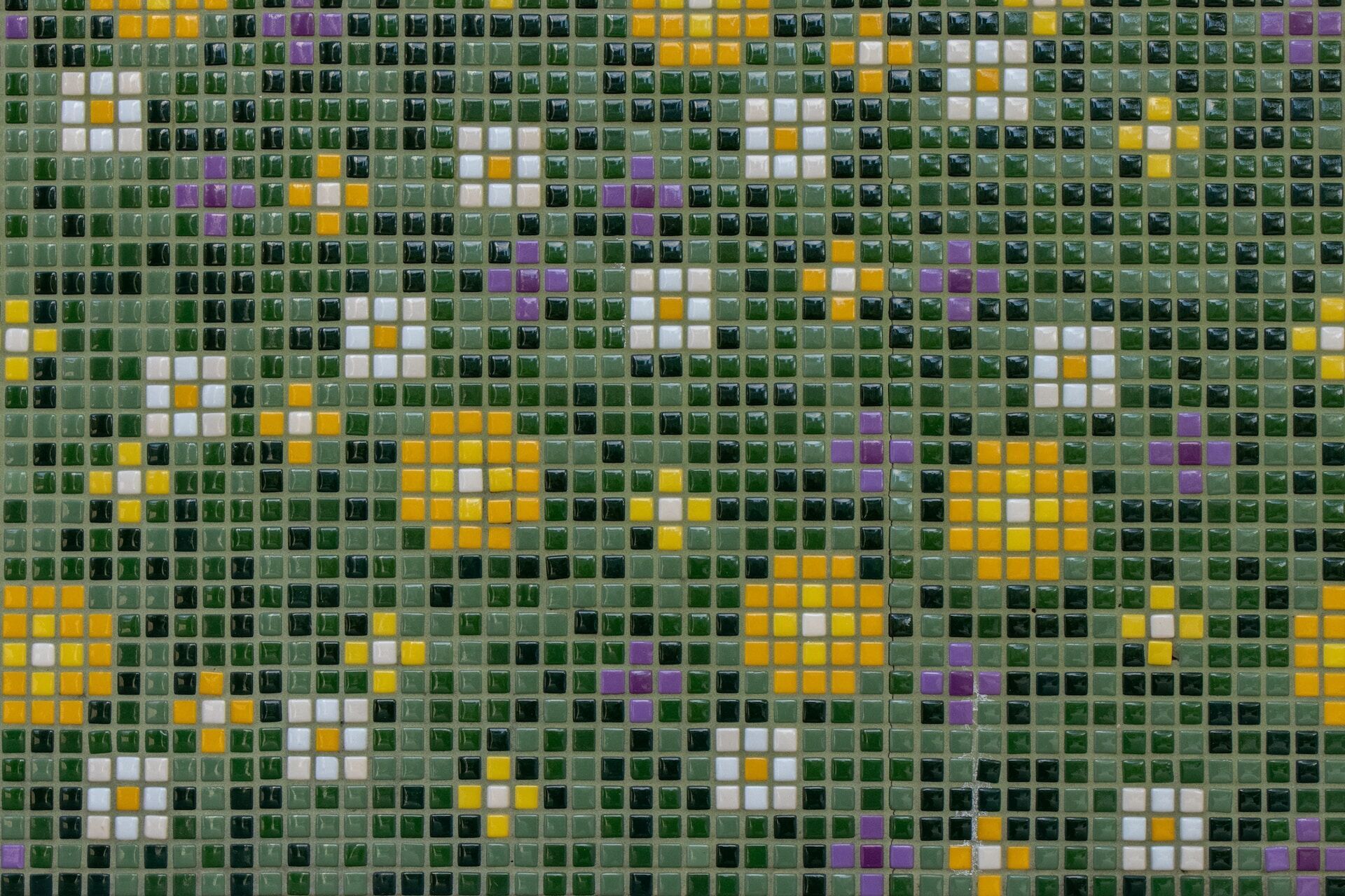 Close-up of a mosaic tile pattern with green, yellow, white, and purple tiles in a floral design