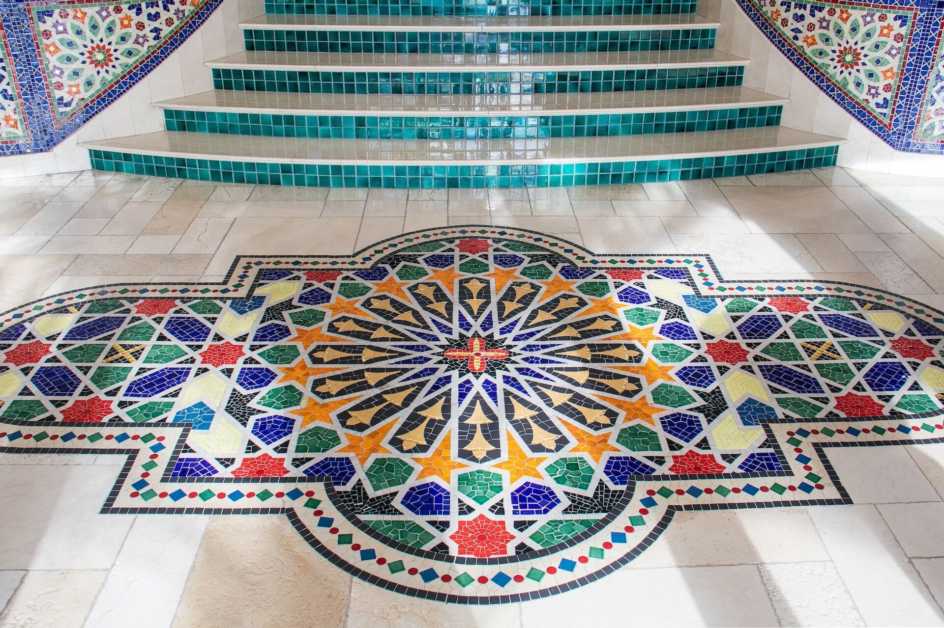 Intricate mosaic tile design on floor with green-tiled stairs in background