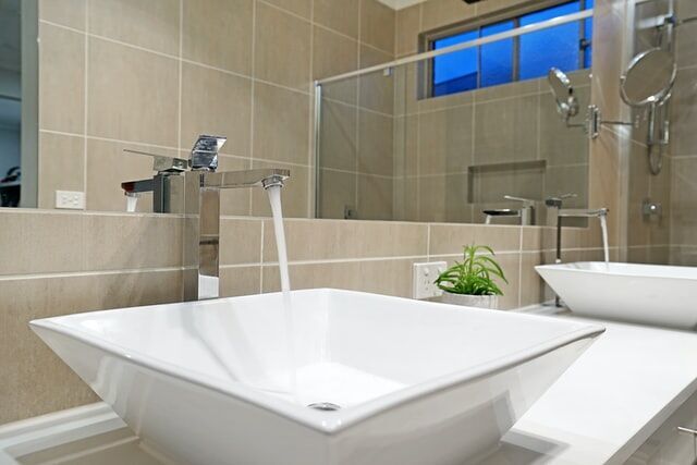 Modern bathroom featuring a white vessel sink, chrome faucet, and beige tiled walls with a small plant