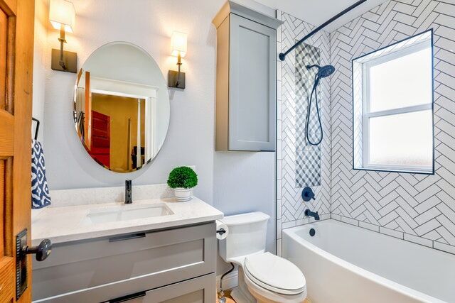 Bathroom with herringbone tile, vanity, round mirror, and bathtub