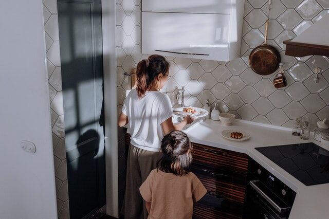Woman and child in a kitchen with a white hexagonal tile backsplash and modern cabinetry