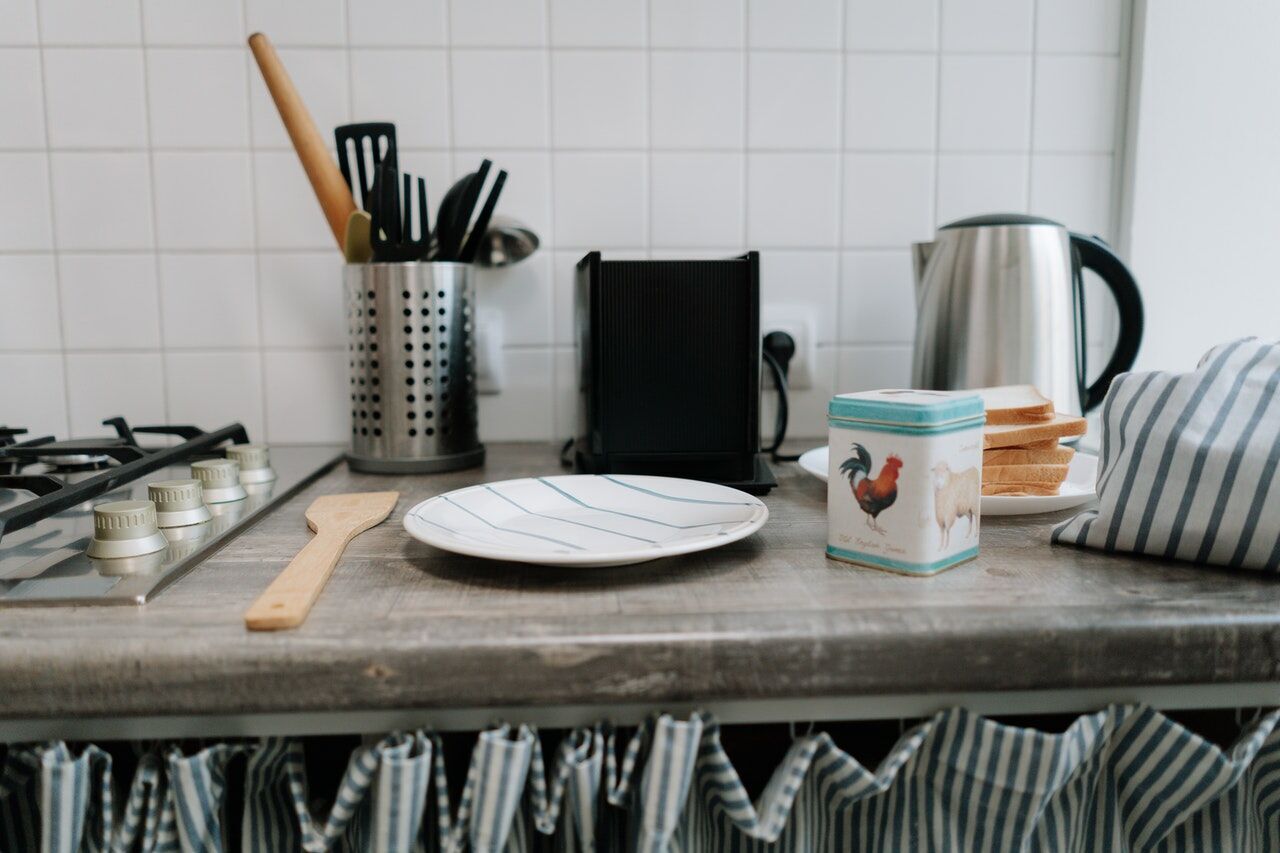 Kitchen counter with wooden spoon, plate, tin container, kettle, toaster, and tiled backsplash