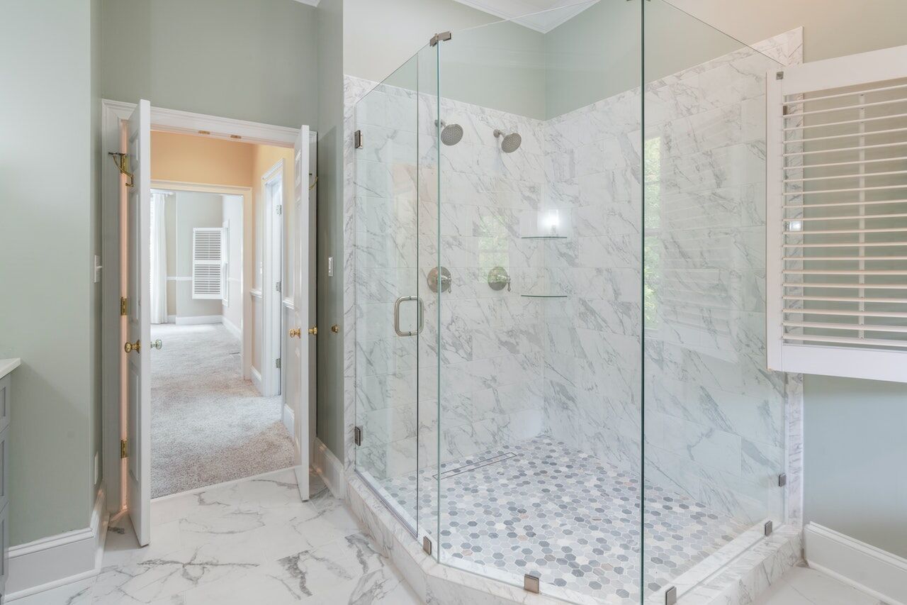 Bright bathroom with glass shower, marble walls, and hexagonal tile floor