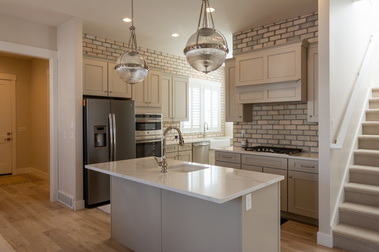 Modern kitchen with a central island, white countertop, stainless steel appliances, and brick backsplash
