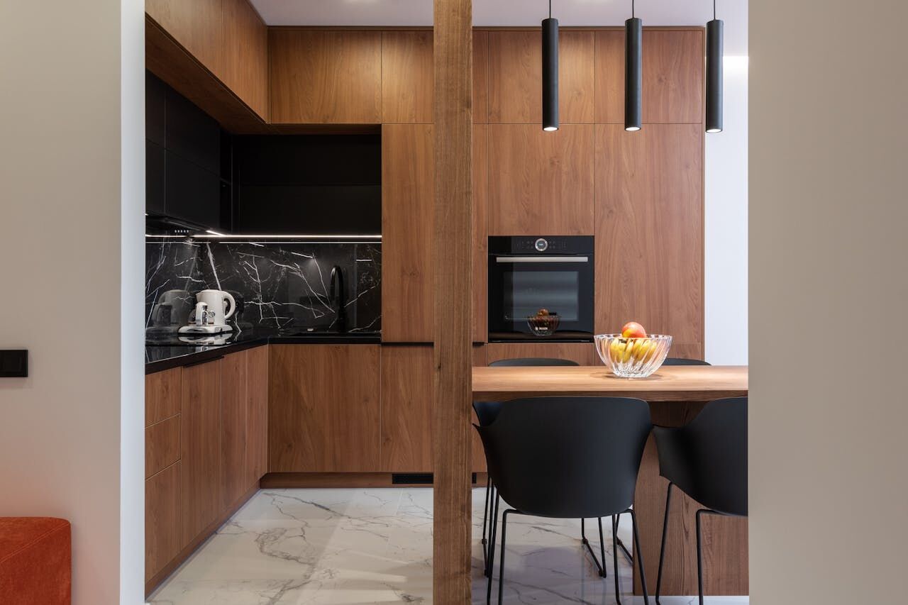 Modern kitchen featuring wooden cabinets, black marble backsplash, and dining area with black chairs